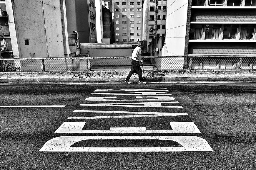 Black and white street photography of man walking on scooter