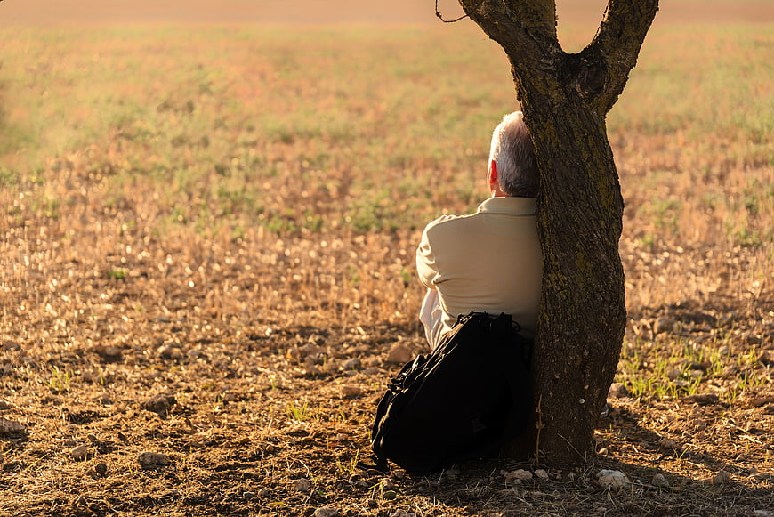 Senior man resting alone under a tree in a field