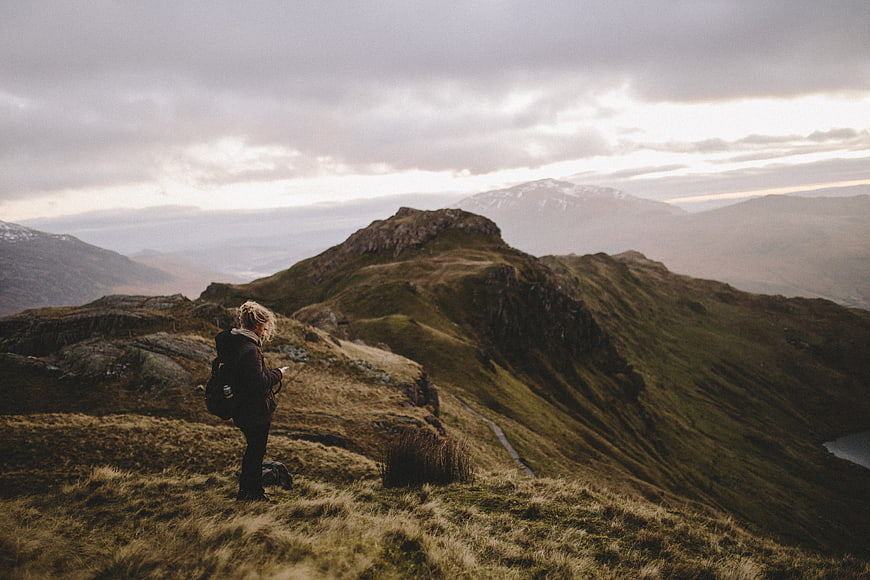 Woman hiker standing on mountain ridge overlooking vast landscape
