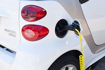 Close-up of white electric car charging with yellow cable