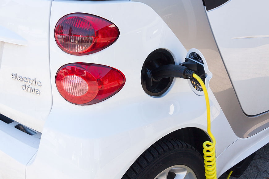 Close-up of white electric car charging with yellow cable