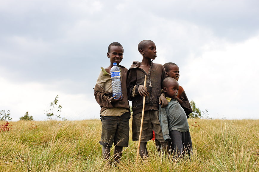 Four African Children Standing In Golden Grassland Holding Water Bottle