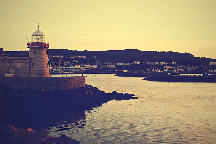 Lighthouse on Harbor Pier at Sunset with Coastal Town