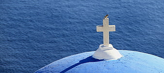White cross on blue dome with bird overlooking the sea