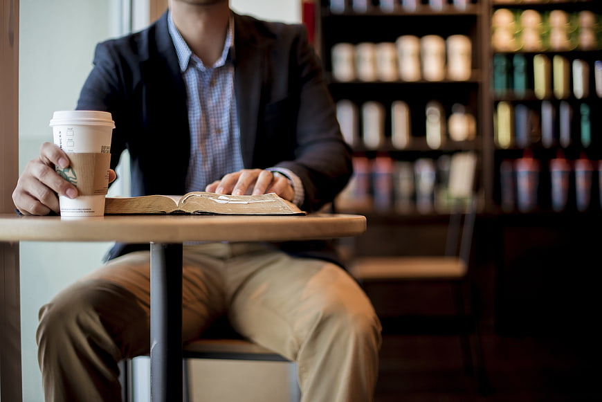 Man reading book and holding coffee cup at cafe table