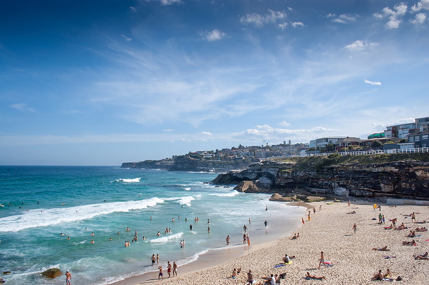 Sunny Beach Scene with Swimmers and Coastal Cliffside Houses