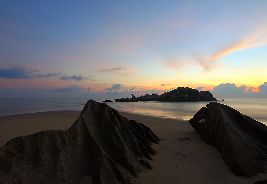 Serene Sunset Beach with Silhouetted Rocks and Smooth Water