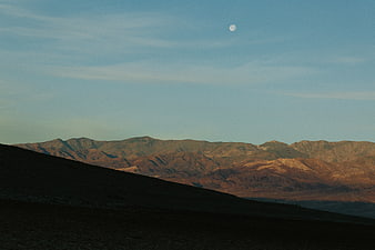 Moon over rugged mountain range at dusk