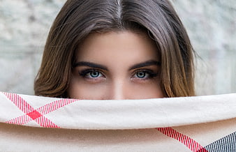 Close-up of woman's blue eyes peeking over plaid blanket