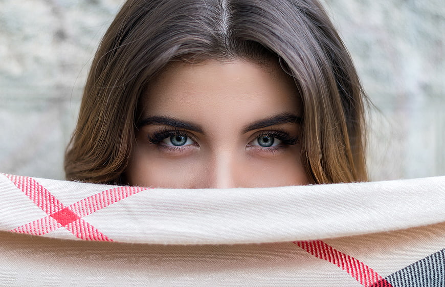 Close-up of woman's blue eyes peeking over plaid blanket