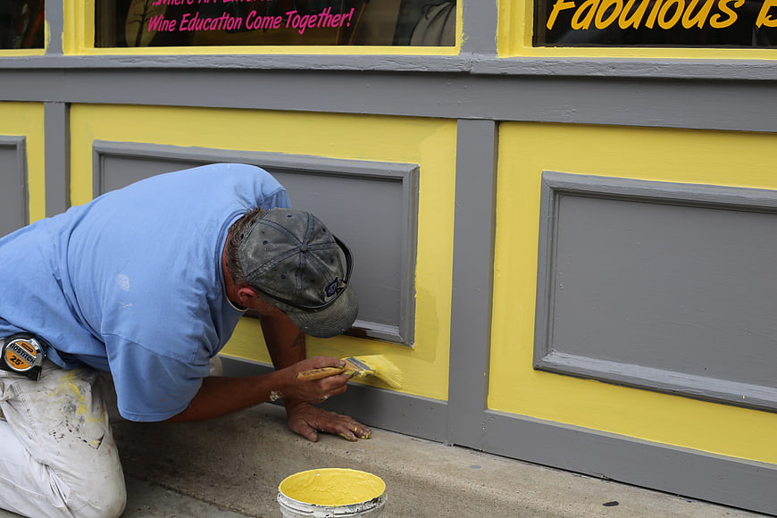 Painter applying yellow paint to building exterior trim