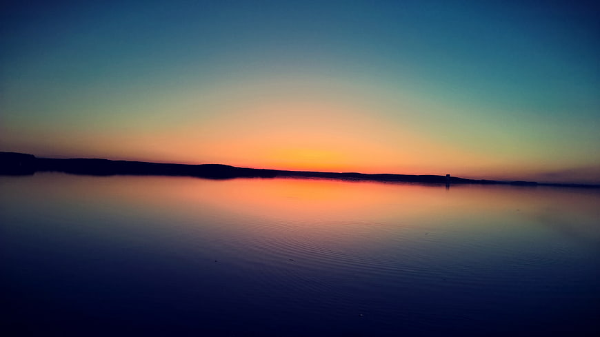 Serene Sunset Over Calm Lake With Silhouette Horizon
