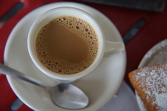Overhead view of cappuccino and powdered beignet on red table