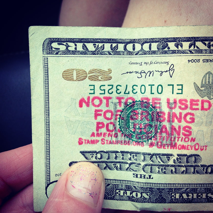 Hand holding stamped twenty dollar bill with political message