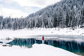 Hiker with Red Backpack Standing by Frozen Alpine Lake in Winter