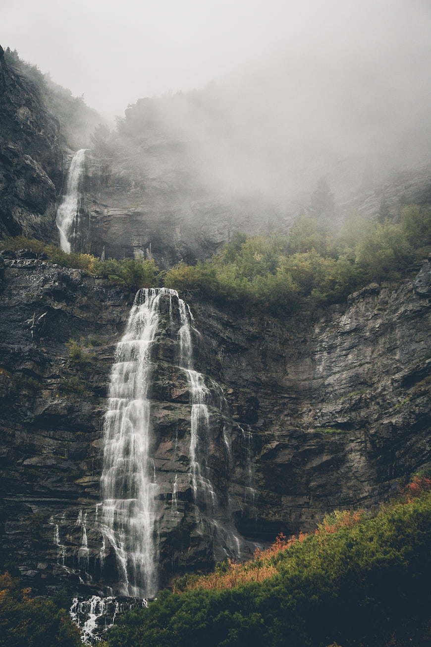 Misty waterfall cascading down rocky cliff in autumn forest