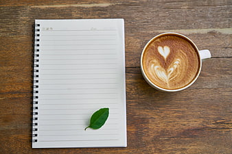 Flat lay of latte with heart art and notebook on wood