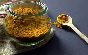 Turmeric powder in glass jar with wooden spoon on dark background
