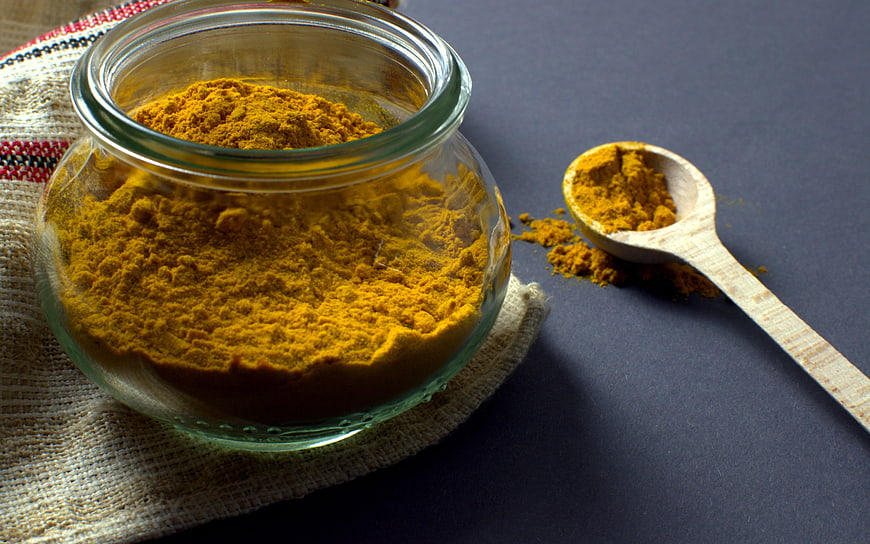 Turmeric powder in glass jar with wooden spoon on dark background