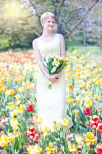 Young woman in yellow dress holding tulips in a spring flower field