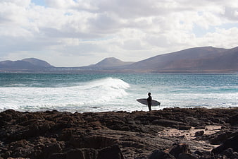 Surfer with board on rocky volcanic coast