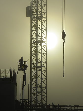 Silhouette of Construction Crane and Worker Against Hazy Sun