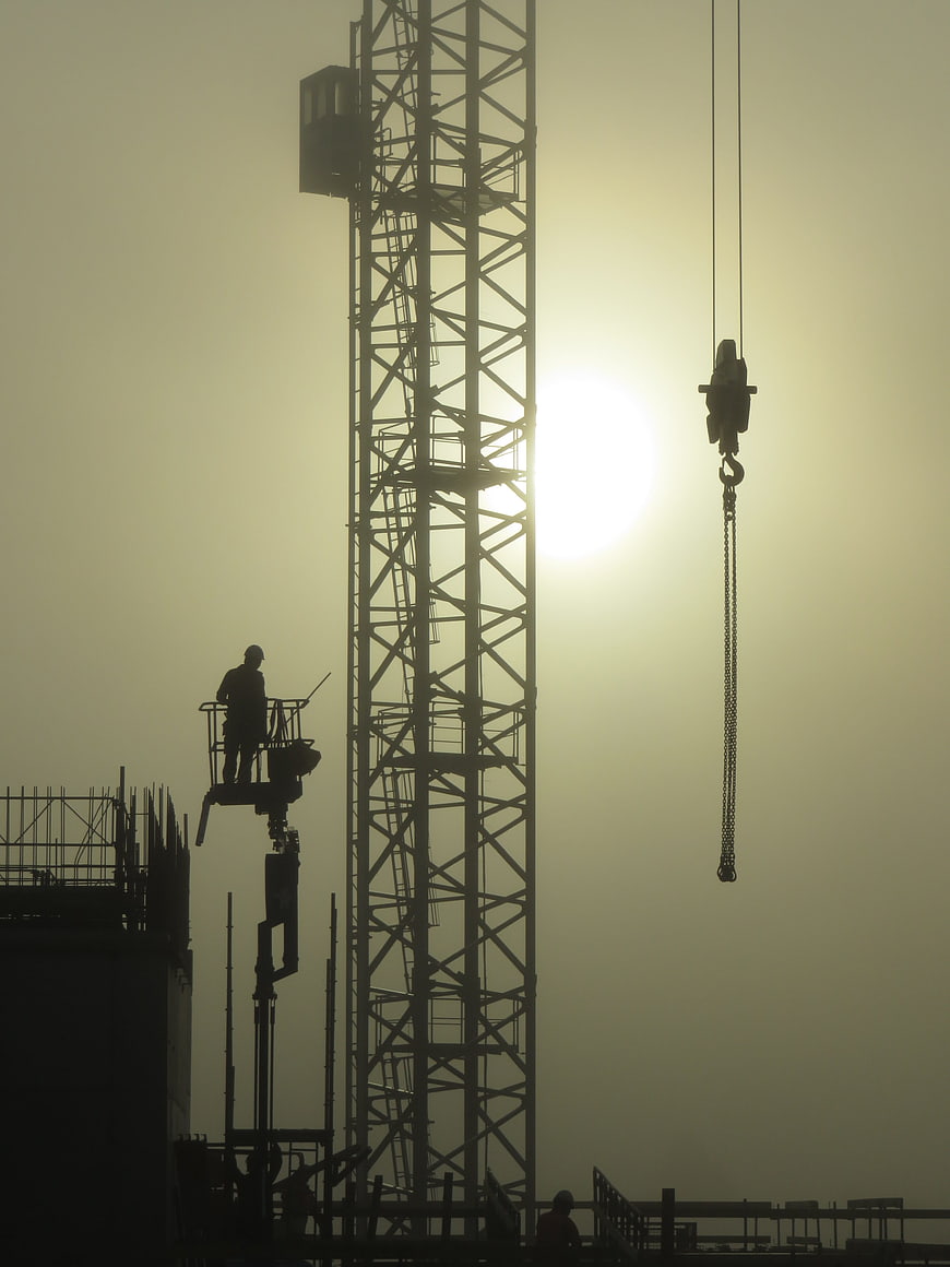 Silhouette of Construction Crane and Worker Against Hazy Sun