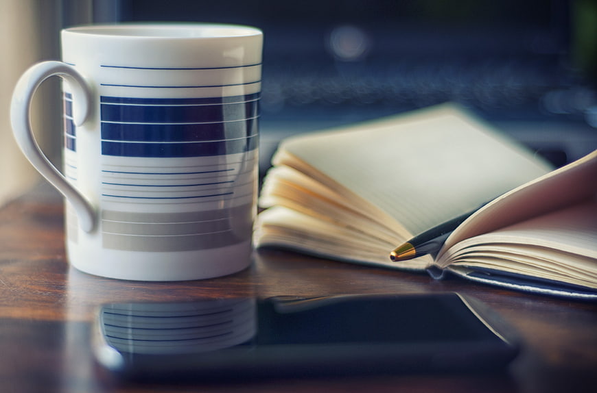 Coffee mug, notebook, and smartphone on wooden desk