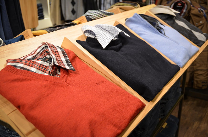 Folded Men's Sweaters And Shirts On Wooden Retail Display Shelf