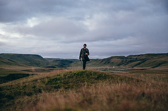 Man hiking on grassy hill in moody landscape