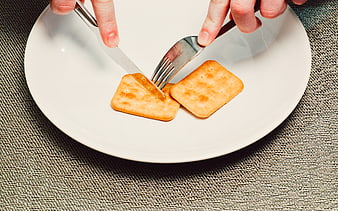 Hands Cutting Crackers with Knife and Fork on White Plate