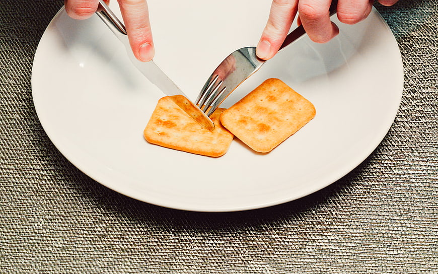 Hands Cutting Crackers with Knife and Fork on White Plate