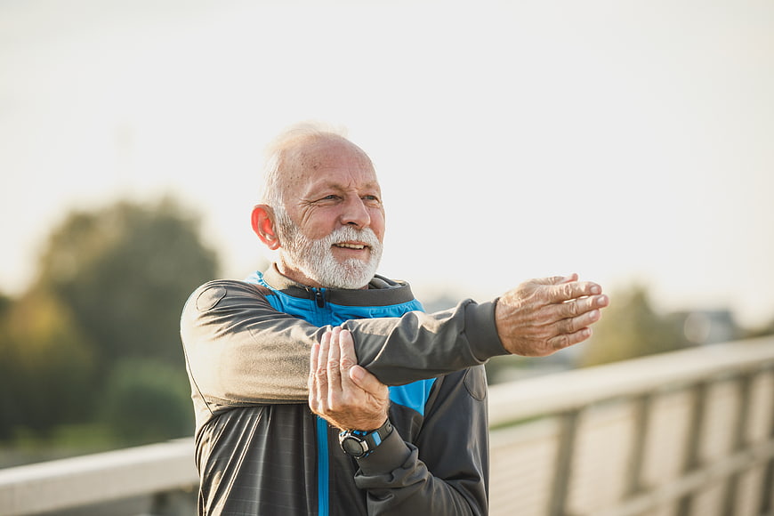 Senior man stretching arm outdoors on bridge