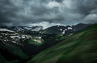 Dramatic mountain landscape with snow patches and stormy clouds