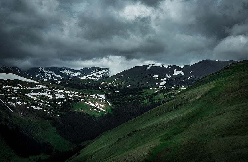 Dramatic mountain landscape with snow patches and stormy clouds