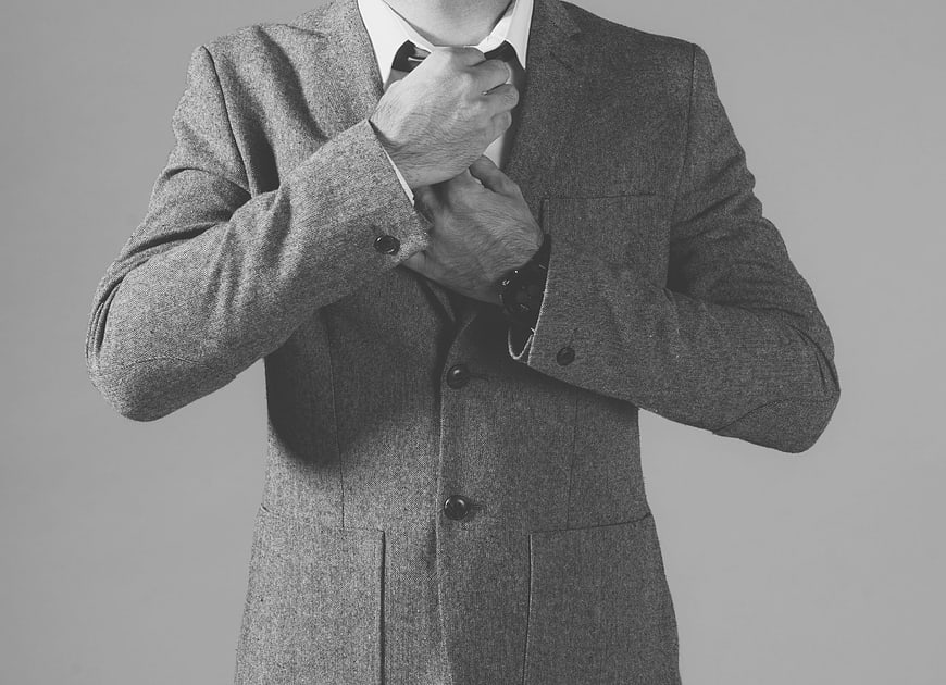 Man adjusting tie in gray wool suit jacket