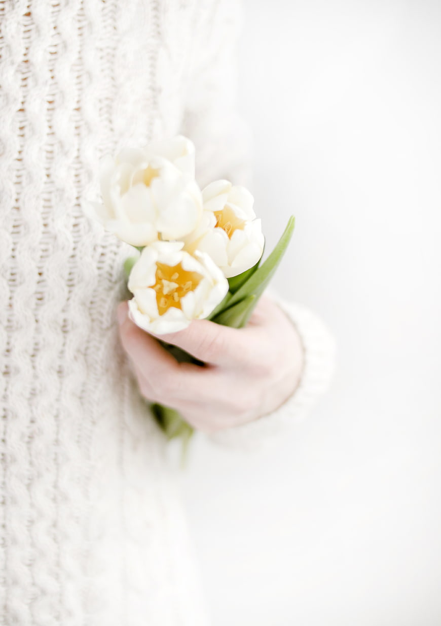 Woman holding white tulips in cozy knit sweater