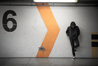 Man in Black Hoodie Leaning Against Concrete Wall with Orange Stripe