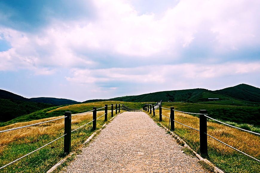 Gravel path through green mountain landscape with wooden fence