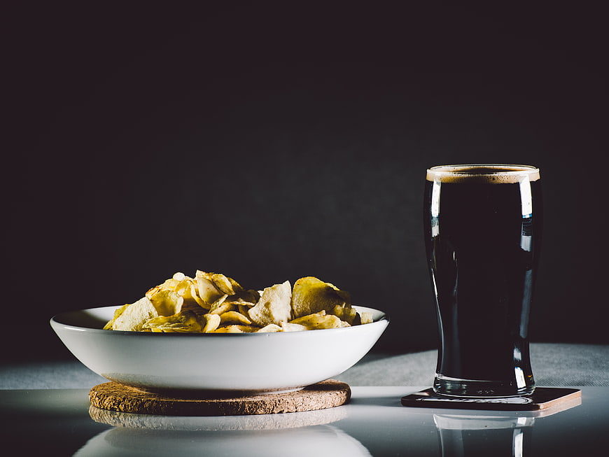Dark beer and potato chips on a reflective table