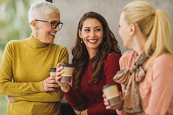 Three smiling women drinking coffee and talking in office
