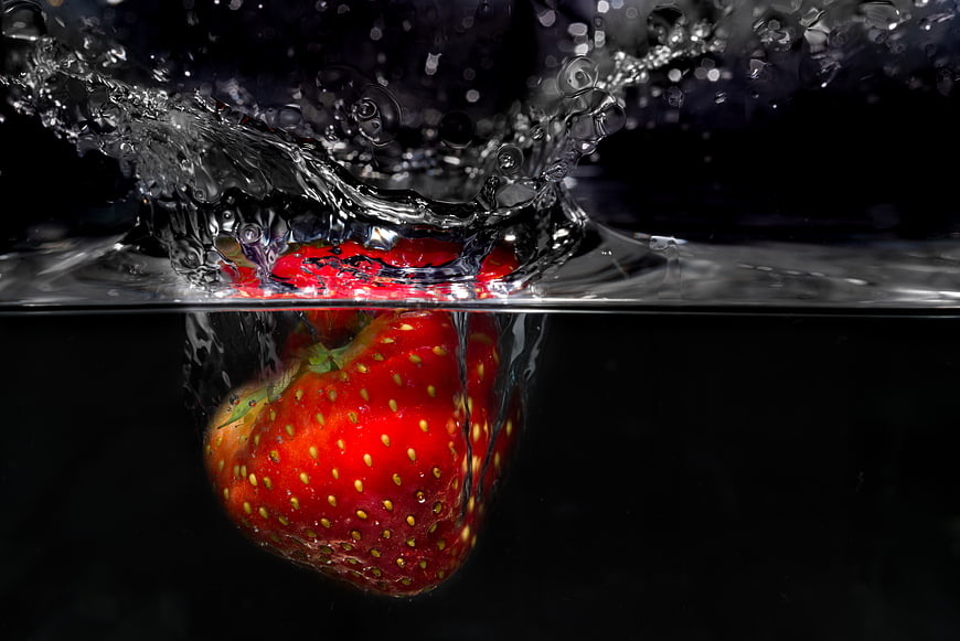 Fresh Strawberry Splashing into Water on Black Background