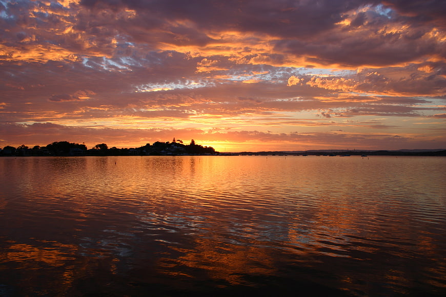 Dramatic orange sunset over calm lake with silhouetted shoreline