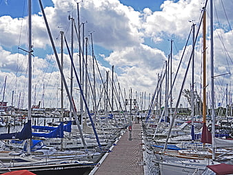 Sailboats docked in marina with blue sky and clouds
