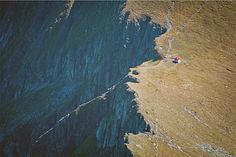Aerial view of tiny red hut on steep mountain cliff edge