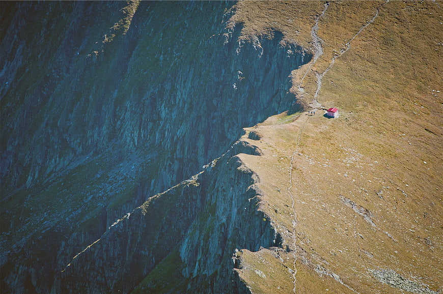 Aerial view of tiny red hut on steep mountain cliff edge
