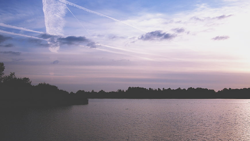 Serene Lake Sunset with Contrails and Tree Silhouette