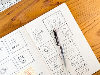 Hand-drawn UI wireframes in notebook on wooden desk