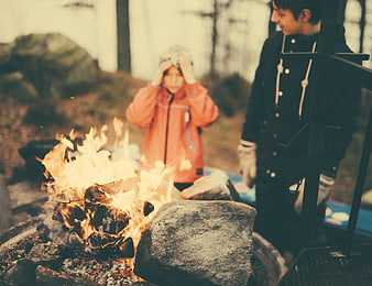 Children warming by campfire in forest