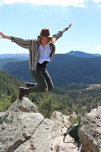 Woman jumping on mountain peak with arms outstretched